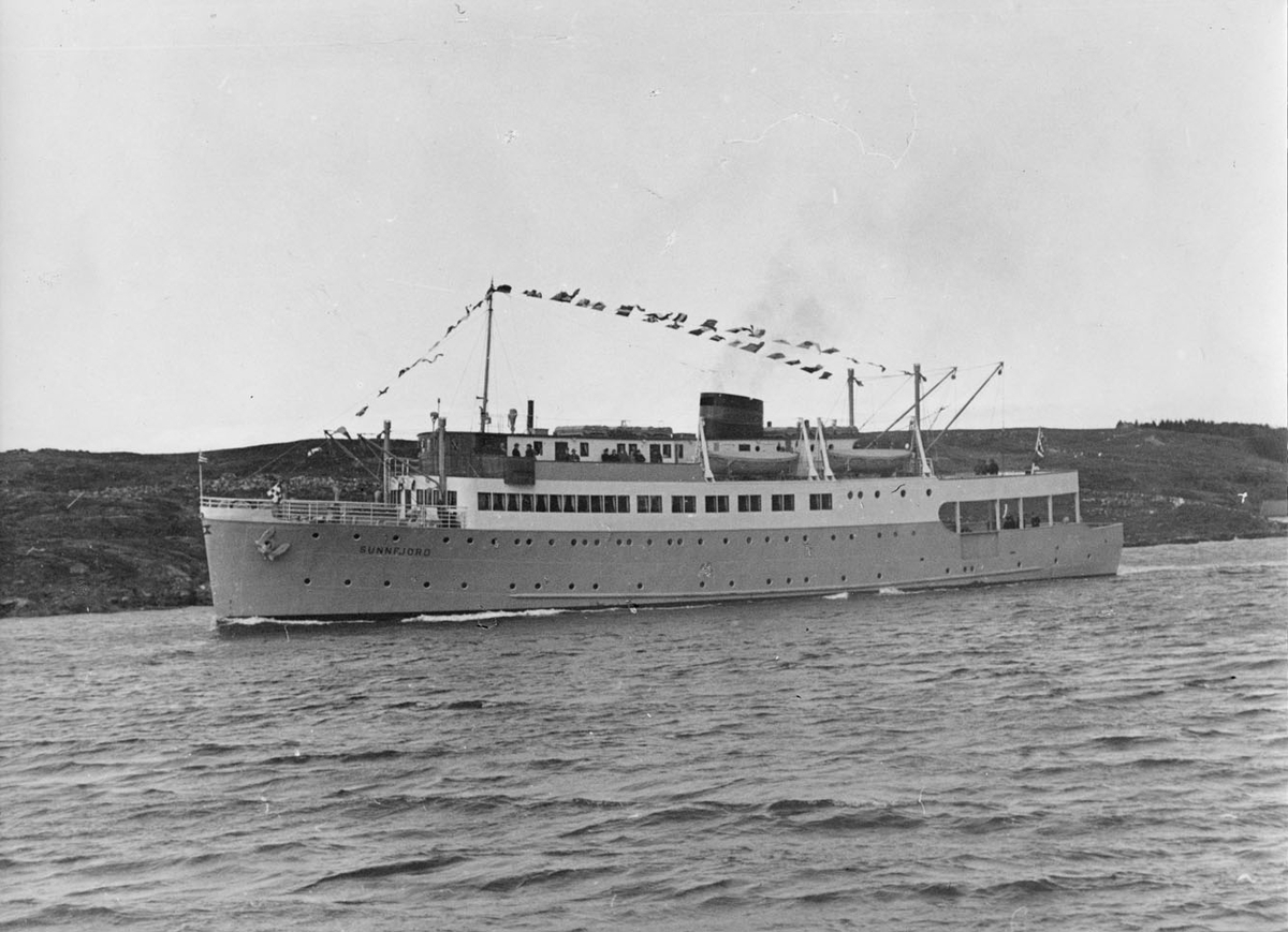 MS SUNNFJORD (bygget 1943), kystlandskap i bakgrunnen og passasjerer på dekk.