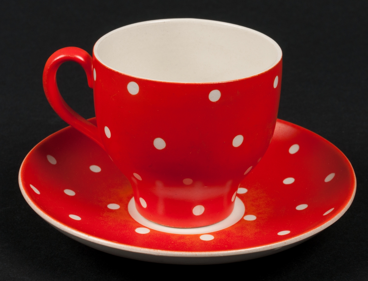 Kaffefat (med tillhörande kopp och assiett) tillverkad vid Gefle Porslinsfabrik AB. Röd bottenfärg med vita prickar. Dekorens namn "Amanita" formgiven av Helmer Ringström. Koppens modell förmodligen formgiven av Arthur Percy.