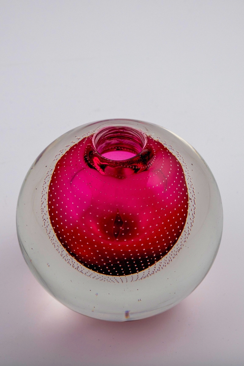 Glassvase i underfangsteknikk. Eggeformet koprus med et rosa sjikt innerst, omgitt av en tykk klar glassmasse. Liten sirkulær åpning. Korpus er dekorert med rekker av små luftbobler som danner et spiralformet mønster.