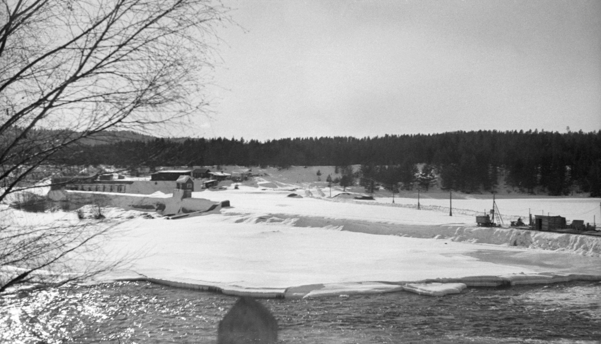 Kraftverksdammen ved Skjefstadfossen i Heradsbygda i Elverum.  Fotografiet er tatt i februar 1942, på et tidspunkt da bare den østre, djupeste og mest vannrike delen av elveleiet (i forgrunnen på dette bildet) var åpent.  Den vestre delen av elveleiet derimot, var is- og snødekt.  Fotografen har stått på Glommas østre bredd med kameraet vendt mot den vestre delen av den buete damterskelen.  Om lag midt på dammen, til høyre i dette bildet, er det reist et par brakker, antakelig i samband med anleggsarbeid som ble gjort vinterstid, da det var liten vannføring.  Vi ser også at det er lagt strøm på midlertidig oppsatte stolper ut mot brakkene, antakelig for å få energi til belysning på arbeidsstedet i den mørke vintersesongen med korte dager.  Til venstre i bildet ser vi inntaksdammen med der turbinrørene som førte vann ned til kraftverket, snaut 500 meter nede ved den vestre elvebredden. 