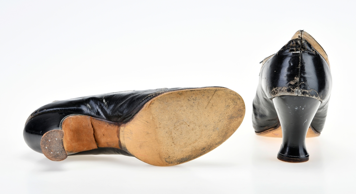 Et par høyhælte damesko med snøring. De er sydd av svart og hvitt skinn. Hoveddelen av skoen er av svart skinn, mens partiet der det er snøring og en kanten langs åpningen er av hvitt skinn. Tåen er avrundet. I front er det 8 par metallmaljer for snøring. Skoene er snøret med svarte, flate skolisser. Under snøringen er det en uforet tunge. Skoene er foret med lerretsstoff og skinn. Innersålen er av mørk brunt skinn. Det har vært tekst på sålen, men den er slitt bort. Yttersålen er av brunt lær. Hælen er av tre og trukket med skinn/lær. Langs kanten på hælen er det en smal sikk-sakk-bord i sølv.