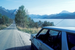 En grusvei går langs fjorden. Fotografens bil, med logoen ti