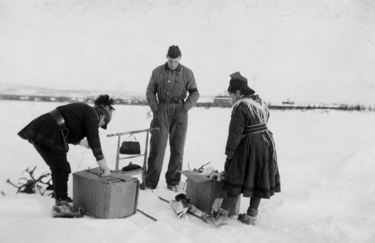 Försäljning av samiska produkter vid en spark. En samisk kvinna och en samisk man visar produkter för en flygmekaniker under övning i Gällivare, 1944.