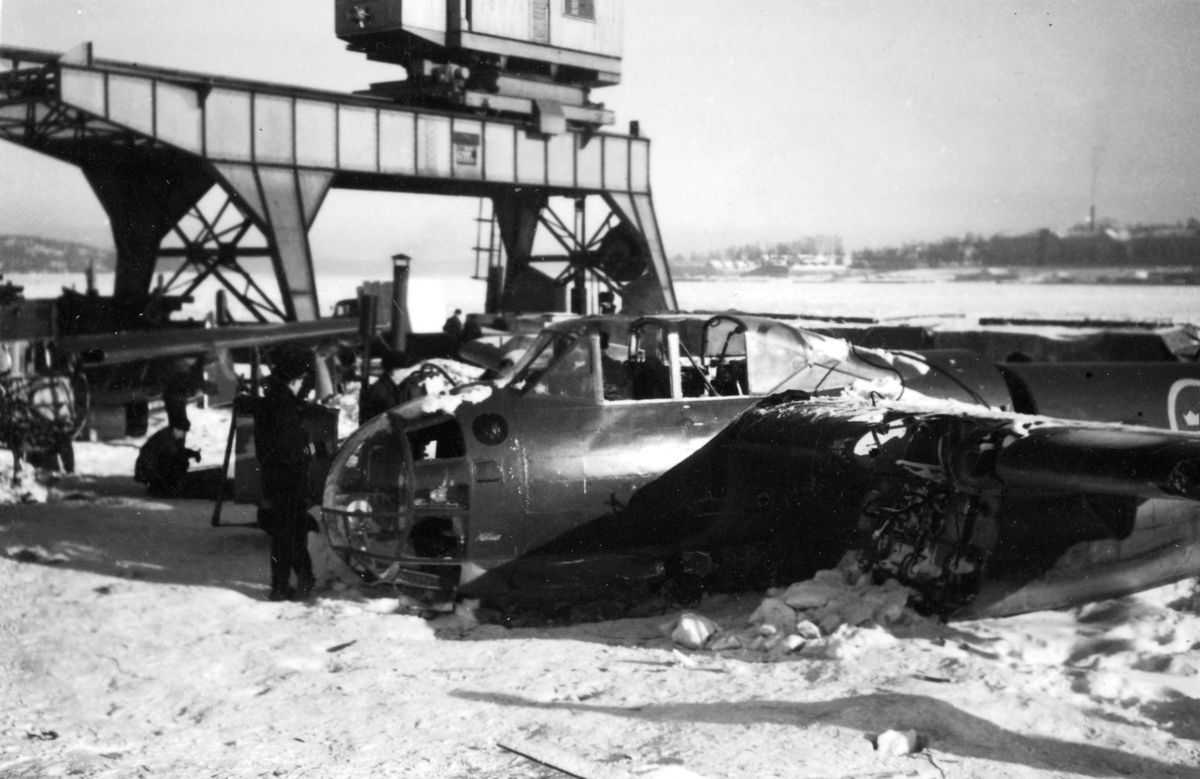 Två bärgade flygplan B 18 ligger på kajen i Härnösands hamn efter nödlandning på isen den 10 februari 1946. Motorerna har demonterats. I bakgrunden syns en lyftkran som användes vid bärgningen.