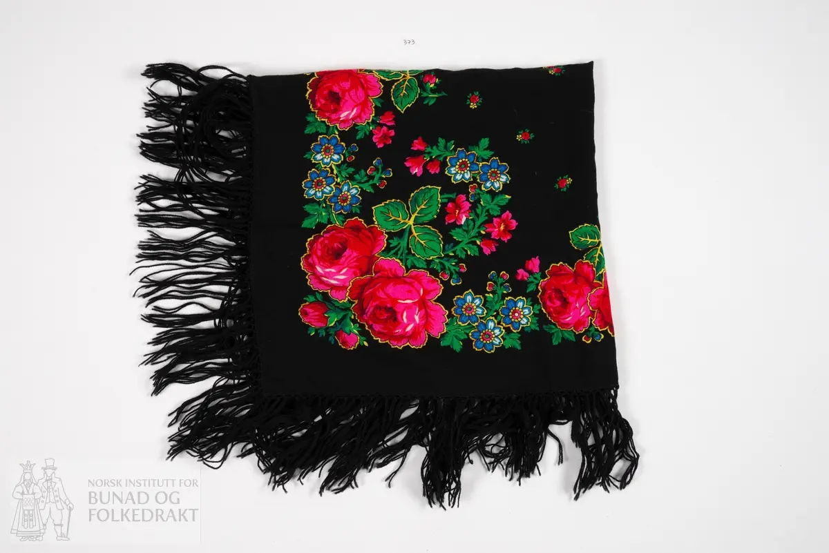 Hodetørkle, svart roseplagg. Av svart ullmuseline, kypertbinding, med trykt blomstermønster i fleire fargar. Smale doble faldar i alle fire sider, sydd med maskin. Påknytta svarte ullfrynser.