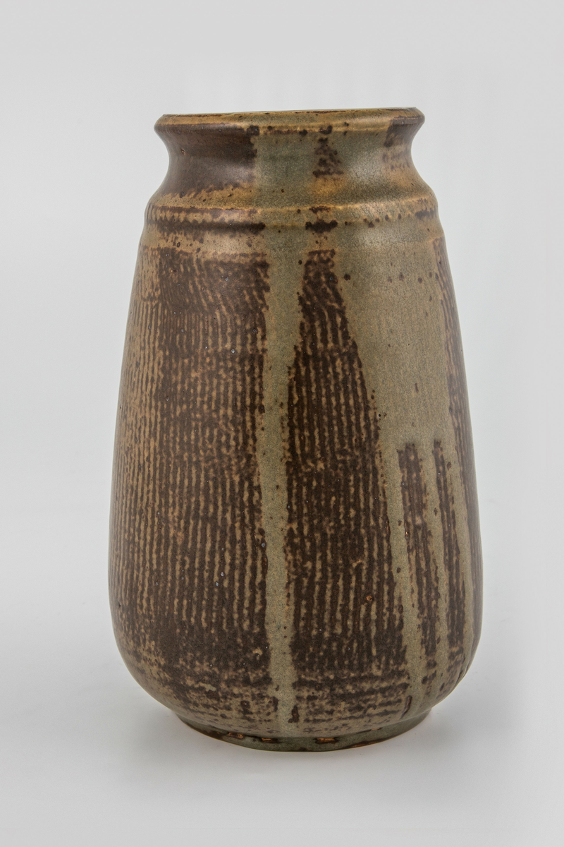 Høyreist vase i glasert steingods. Kjegleformet korpus som hviler på en lav fotring, utoverbrettet munningsrand. Korpus er dekorert med vertikale mørkebrune riller, som på deler av vasen er dekket av en gråbeige flyteglasur.