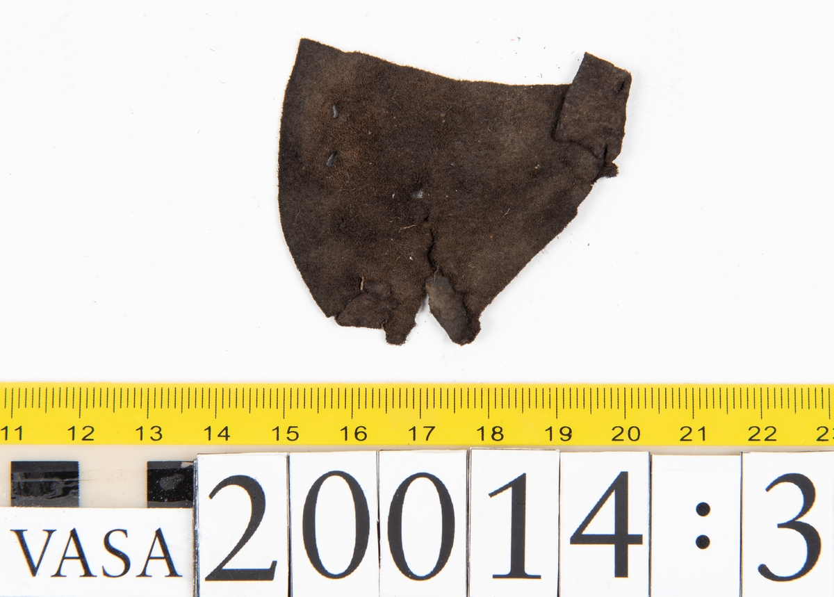 Delar och fragment från skobotten: två inlägg från tå- respektive hälparti, två vikta fragment samt ett flertal mindre fragment. Inläggen har hål efter träpligg. Lädret är mycket sprött.
