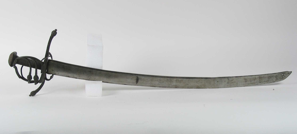 Pyramideformet knapp med strekdekor. Asymmetrisk kurvfeste med to sidebøyler( øverste avbrukket )med riflede fortykkelser på midten. mellom håndbøylen og kurvens ytterkant. Innsiden har en  sidebøyle. Kurvens basis er på utsiden en kvadratisk parérplate med to hjerteformede gjennombrytninger. På innsiden er det en klingebrekker og tommelbøyle. Opp og nedbøyde parérstenger med riflede fortykkelser på endene.
Tregrep med nyere jerntrådvikling.
Enegget krum klinge med 3 hull ipå klingspissen og en smal hulslipning på ryggsiden.Tre smedmerker på venstre side. 