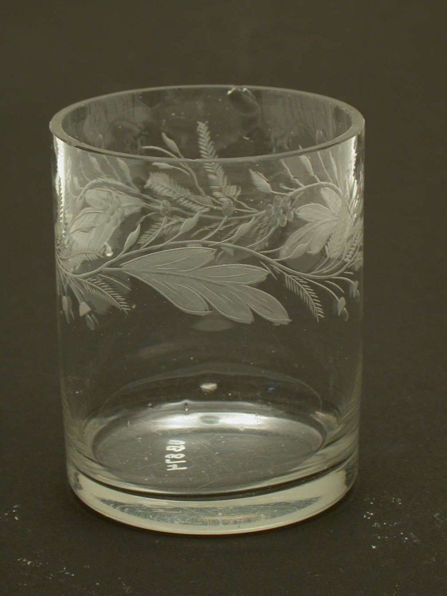 Glass med gravert og olivenslipt blomsterdekor. Det er små hakk i randen på glasset.