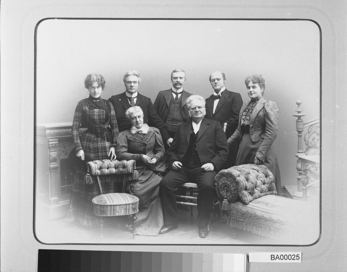 Familieportrett: mor og far sitter i stoler foran, bak i midten de tre sønner, og de to døtre på hver sin side innrammer bilde. Alle ser direkte på betrakteren.
