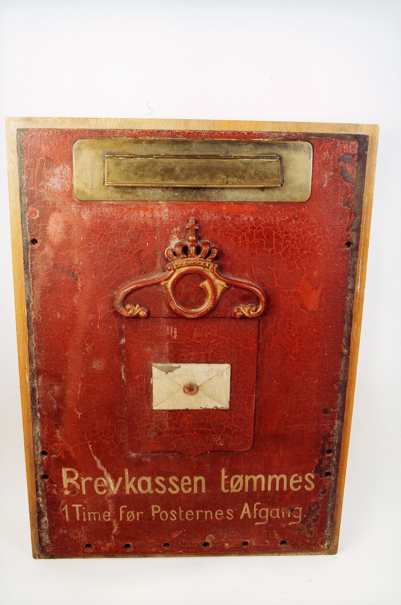 Postkasseskilt av jern, rødmalt. Med tekst "Brevkassen tømmes 1 Time før Posternes Afgang". Posthornemblem med krone.