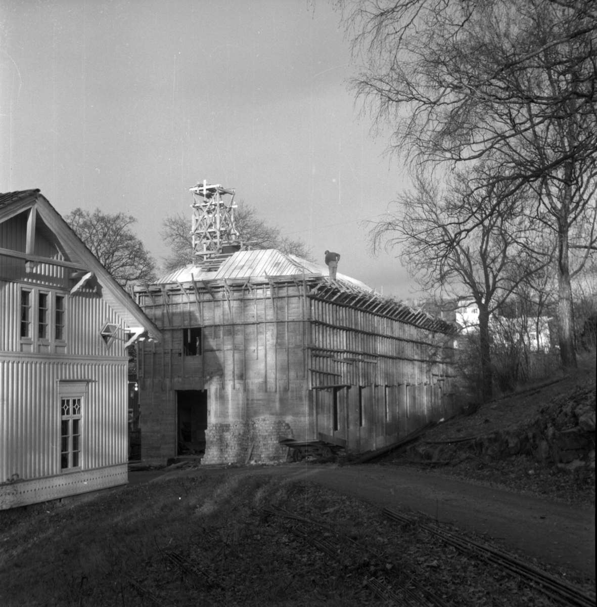 Aust-Agder-Museets første byggetrinn  - senere arkivfløy -  på Langsæ. Under oppføring. Gesims og takarbeid pågår. Mann på taket.
