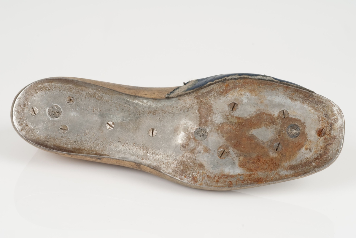 En tremodell i to deler; lest og opplest/overlest (kile).
Venstrefot i skostørrelse 43, og 8 cm i vidde.
Såle i metall.
Lestekam i skinn.