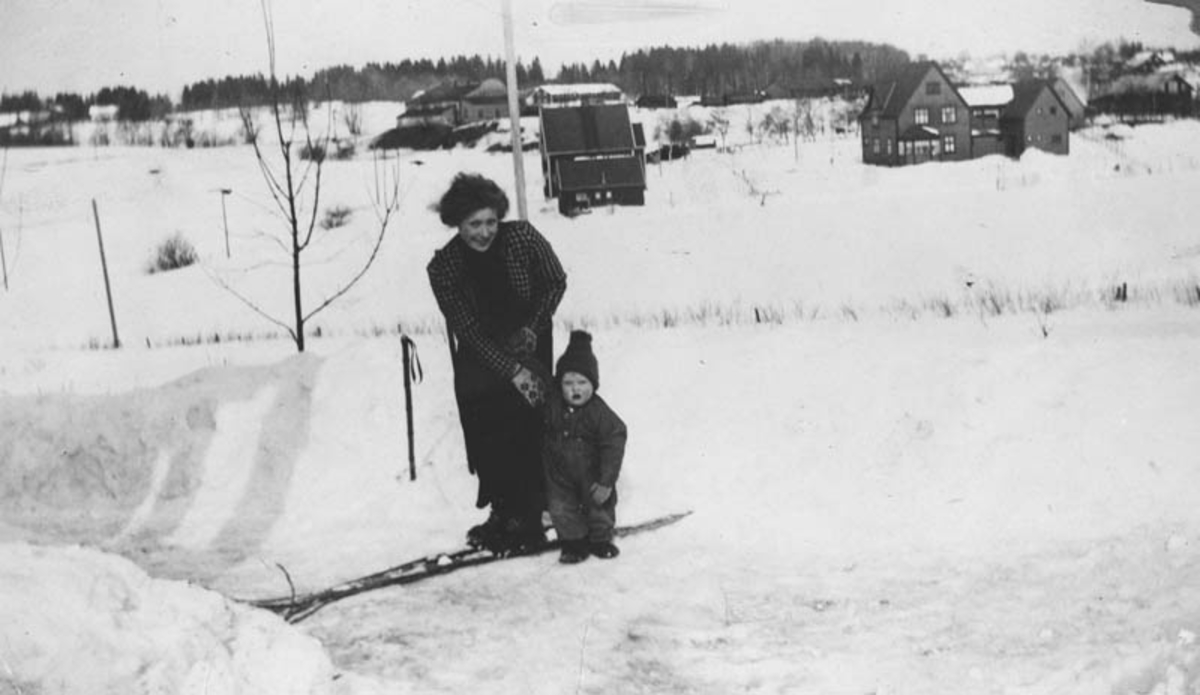 Utsikt mot lokomotivstallen på Ski. Dame med lite barn på ski.