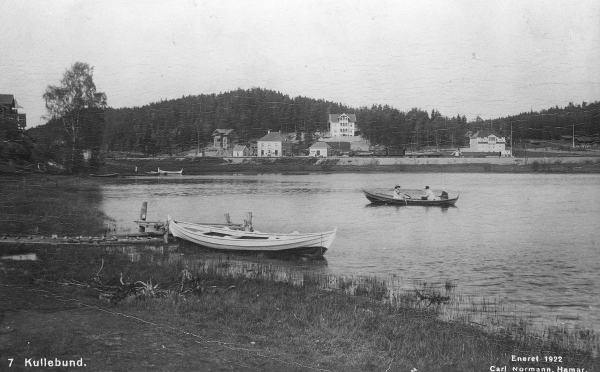 Båt ved brygge på Kolbotntjernet, tre mennesker i robåt. Kolbotn stasjon i bakgrunnen (postkort)