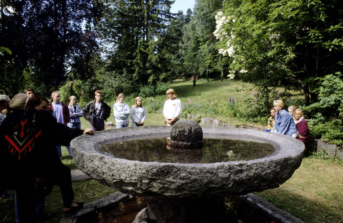 Asker Museum, forsommeren 1996. Hagen: mennesker står rundt en fontene.