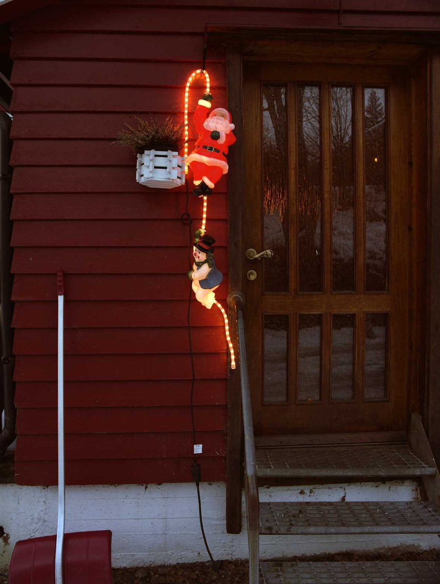 Julebelysning.  

Lysende nisee og snømann klatrer på lysslange ved dørparti på enebolig.