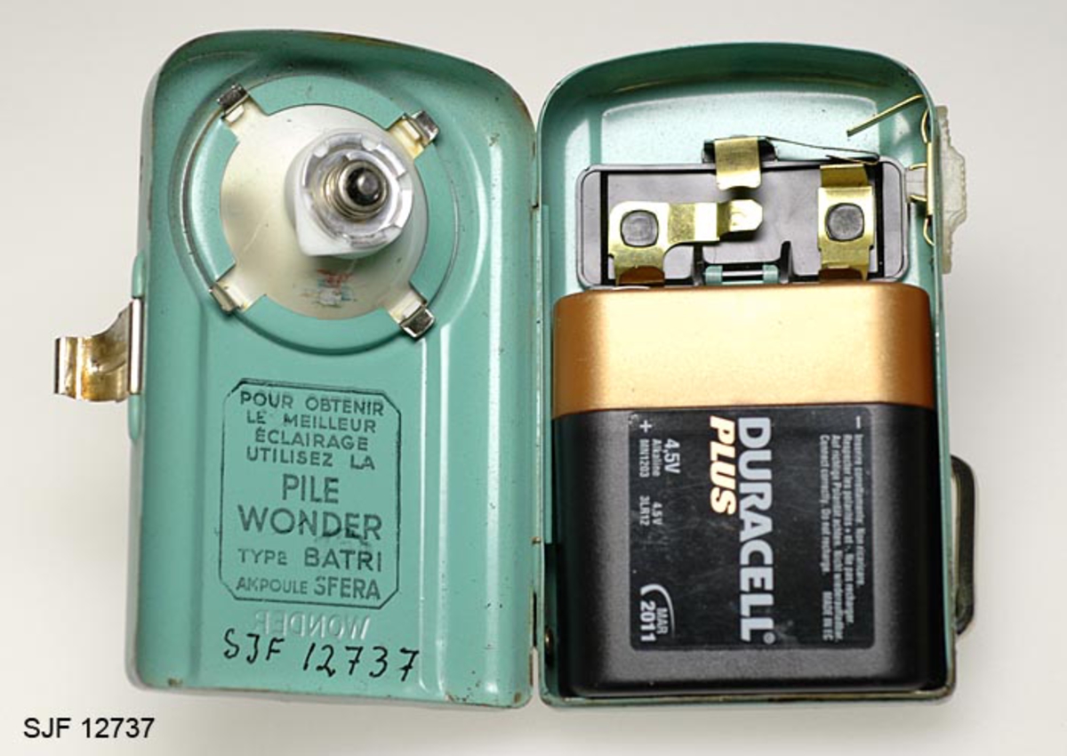 Batteridrevet lommelykt i lakkert metall. Lykta har metallbøyle (støtte) nederst og -hempe øverst. Den er i brukbar stand og ble levert med batteri (Duracell Plus, 4, 5V) som har varighet til mars 2011. 