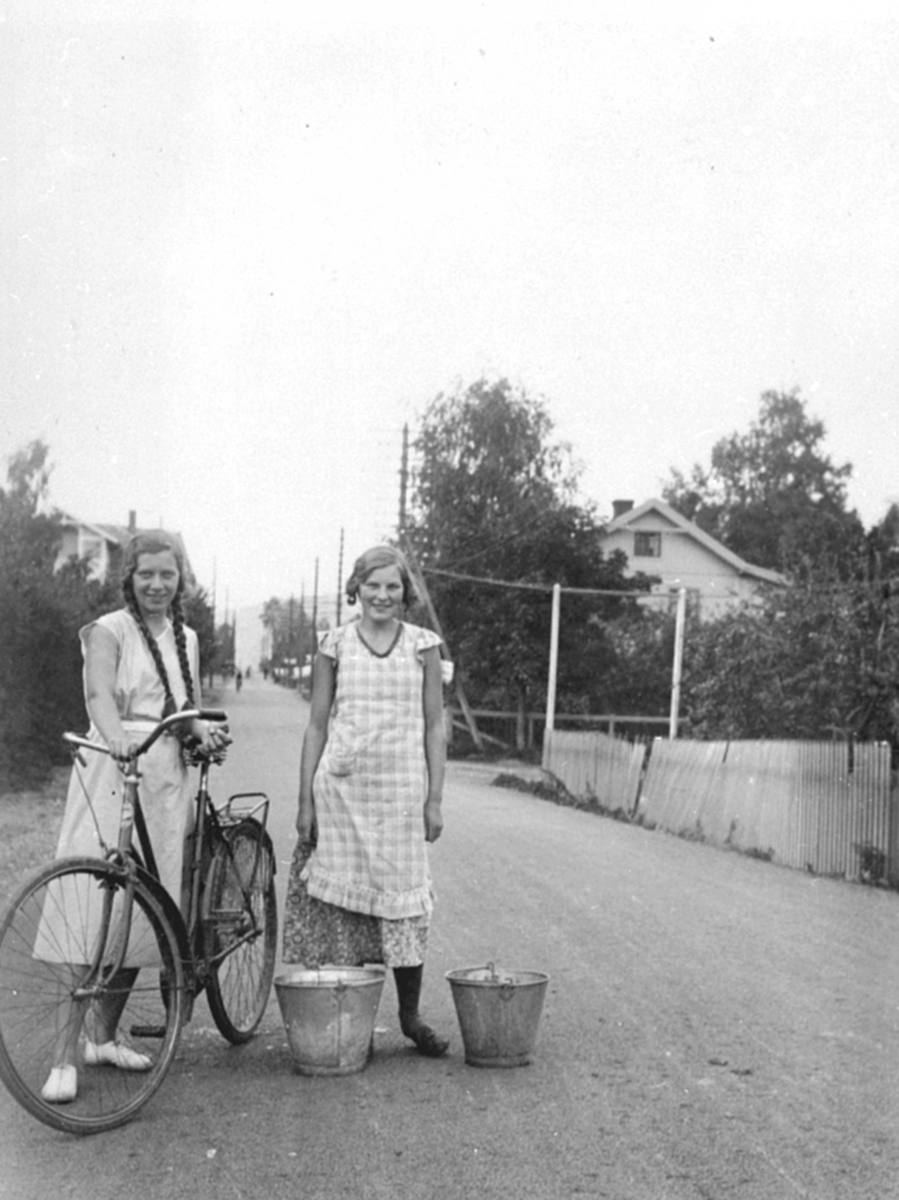 To unge jenter i Storgata, Moelv. Sykkel, sinkbøtter.