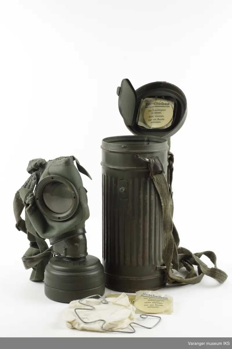 Komplett utstyrt Wehrmact model 1938 gassmaske-sett. Maske og stropper i tøystoff. Brillekomponter i plast. Nederst i beholderen, en tøyduk ca. 20x25 cm beregnet til brillepuss. På underside av topplokk, et lukket rom med 3 par ekstra brilleglass.