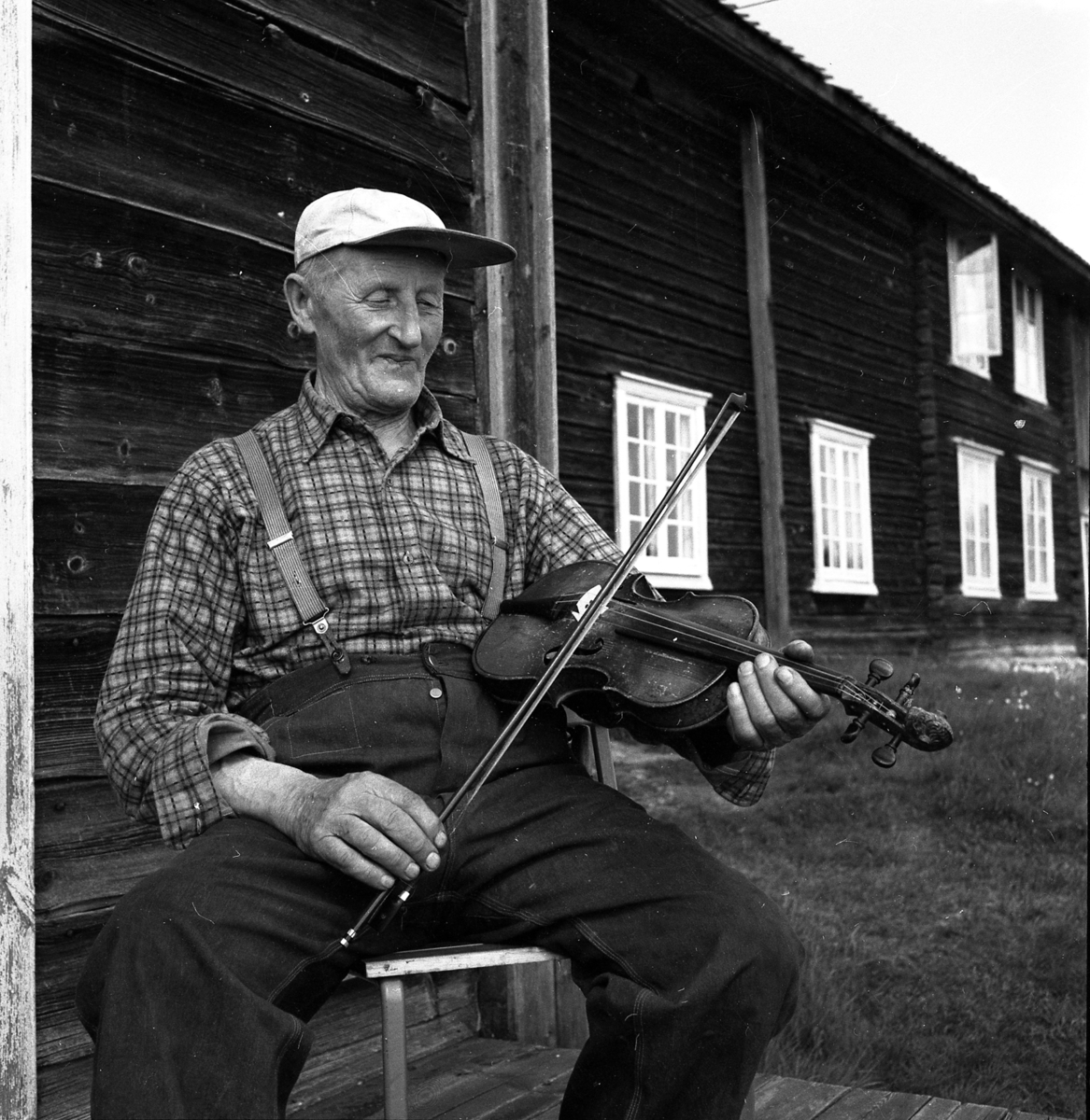 Mann med fele sitter på en stol foran et våningshus. Olaf Lindtorp med Porkkalafela på Tvengsberget sommeren 1953. 