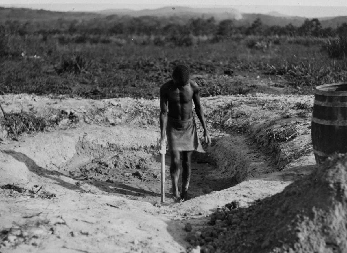 Fra Uganda. En innfødt står i en grop med en spade.