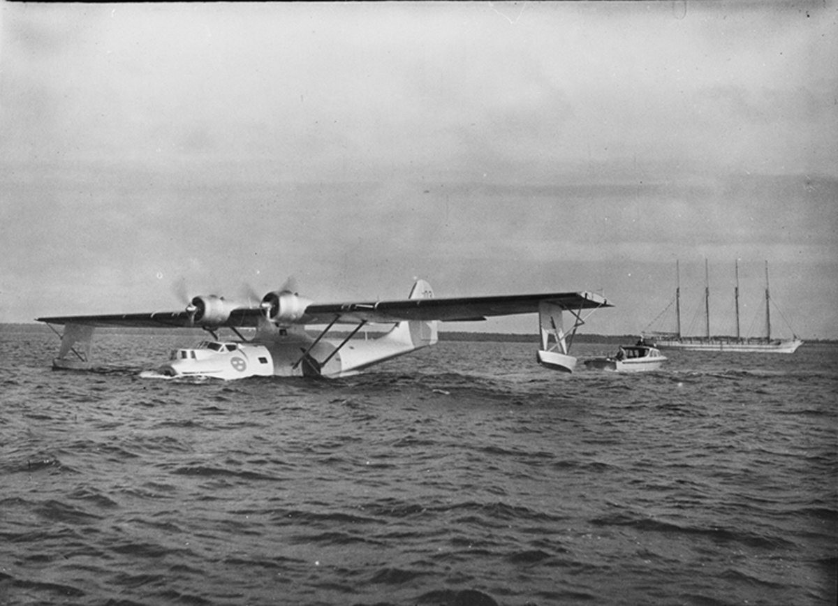 Flygplan TP 47 003 Catalina på vatten. I bakgrunden en båt och ett fartyg.