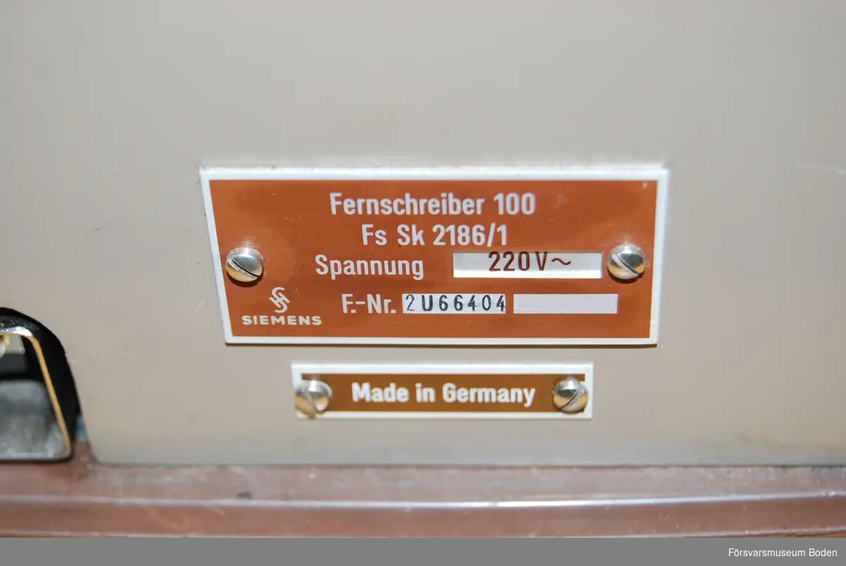 Står på rullbord, transportlådan saknas. Ursprungsbeteckning Siemens typ 100, individnr 2 U 66404. Pappersrulle och remsa är monterade. Enligt etiketter inuti locket var sista översyn 14/1 1982, och föregående 08 1974. Har använts vid AF 1 i Boden.