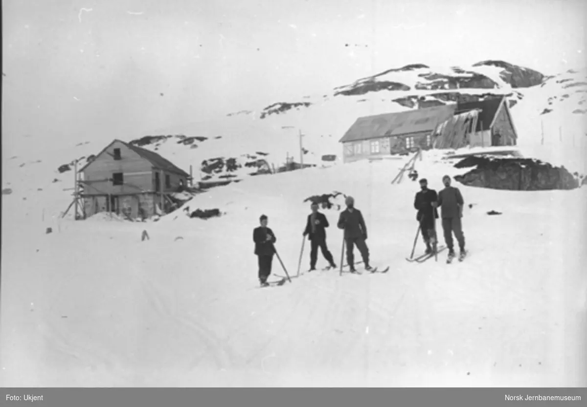 Bergensbanens anlegg; menn på ski med brakker på Hallingskeid i bakgrunnen