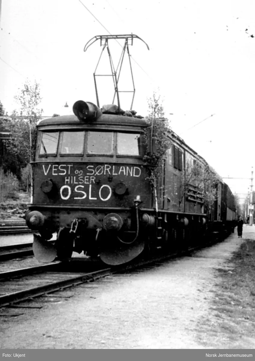 Elektrisk lokomotiv i tog 706 pyntet løv og påskrevet "Vest og Sørland hilser Oslo"
