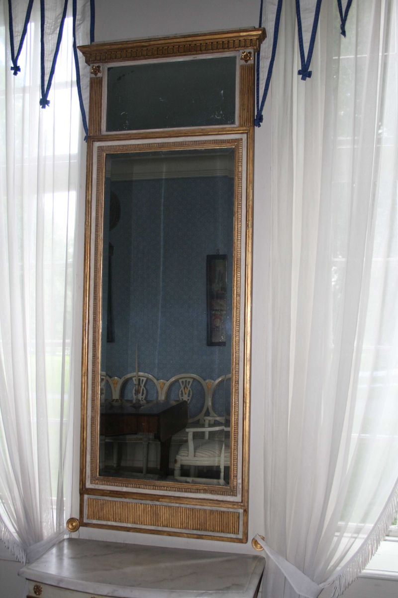 Speil med tilhørende konsollbord, hvitmalte med forgylt dekor og forsiringer. To-delte speil, det lille speilfeltet øverst er dekorert med påmalt urnemotiv.