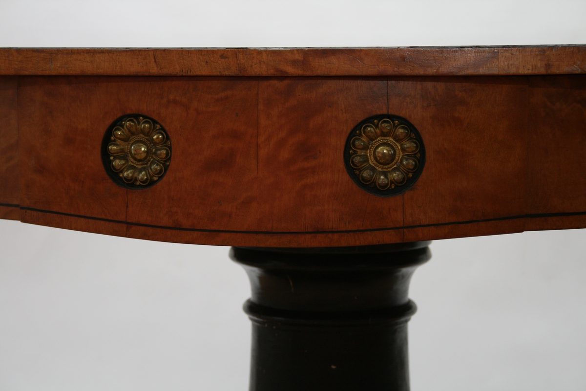 Stort, ovalt bjerketres klaffebord med sort søyle og messing ornamenter, sort kant rundt bordplaten og rundt foten.
Biedermeier.