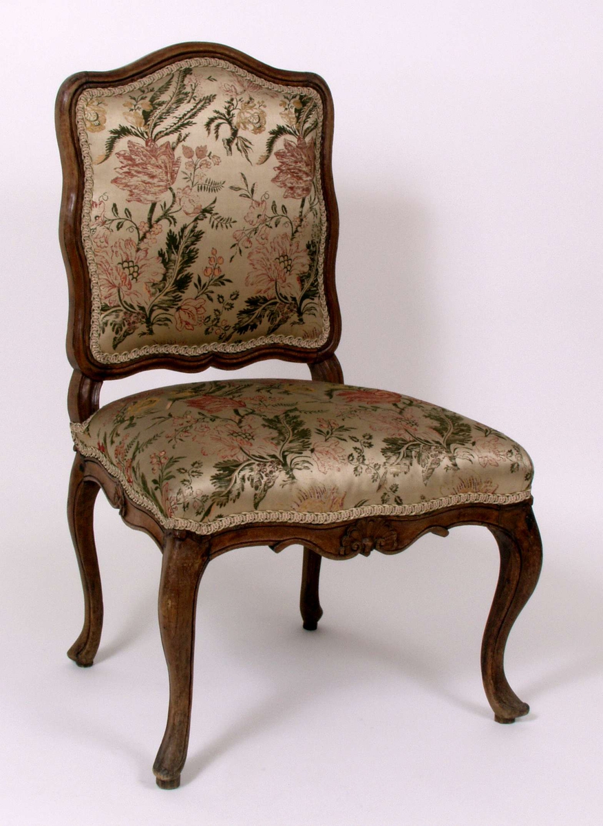 Trestol med polstring i rygg og sete med flerfarget silkedamask og pyntebånd langs tekstilkantene. Blomstermotiv i tekstilvev og dekorative utskjæringer i treverk.
