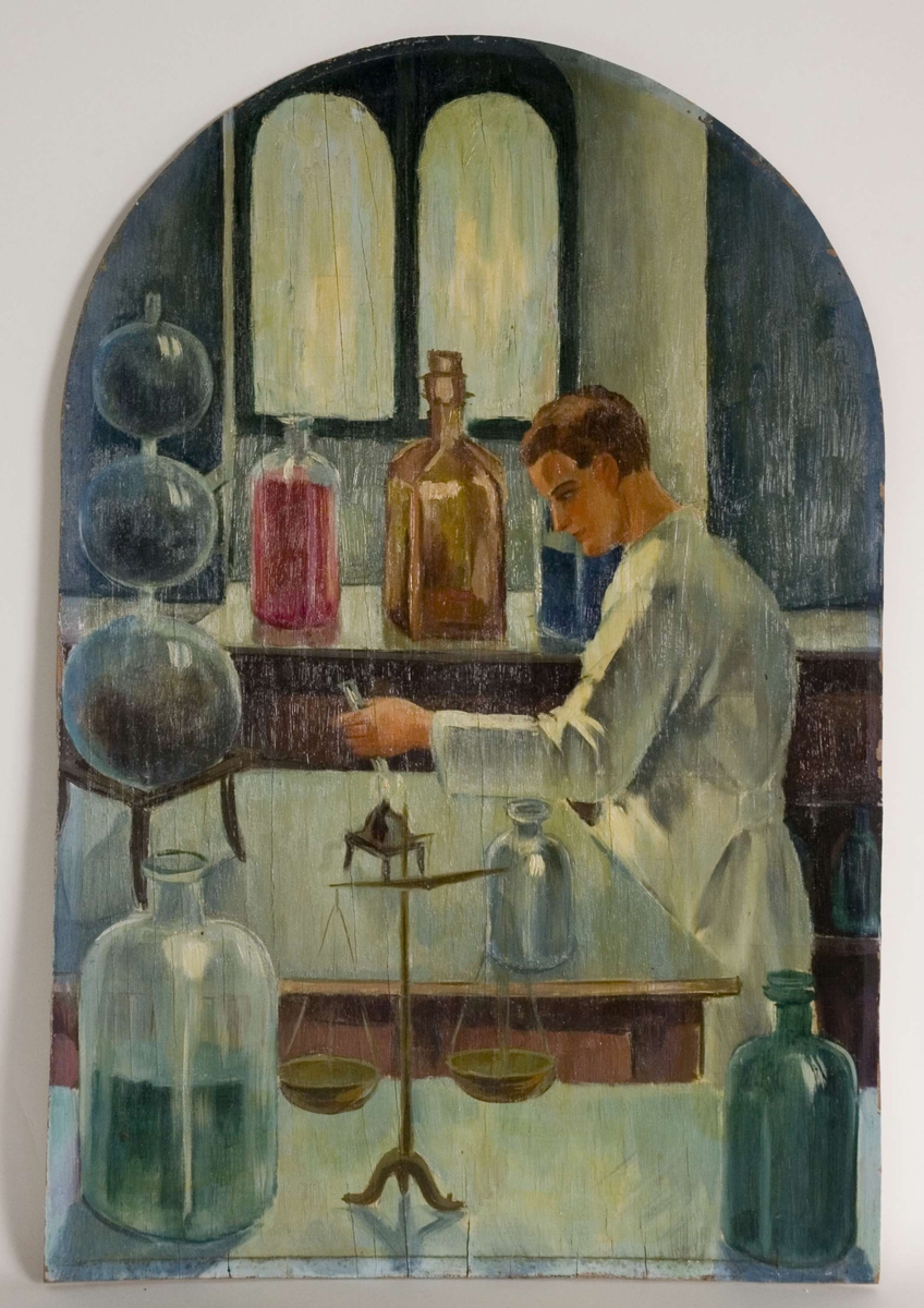 Laboratorieinteriør med kolber, flasker m.m. Skålvekt i forgrunnen. Mann i hvit frakk holder reagensglass over flamme.