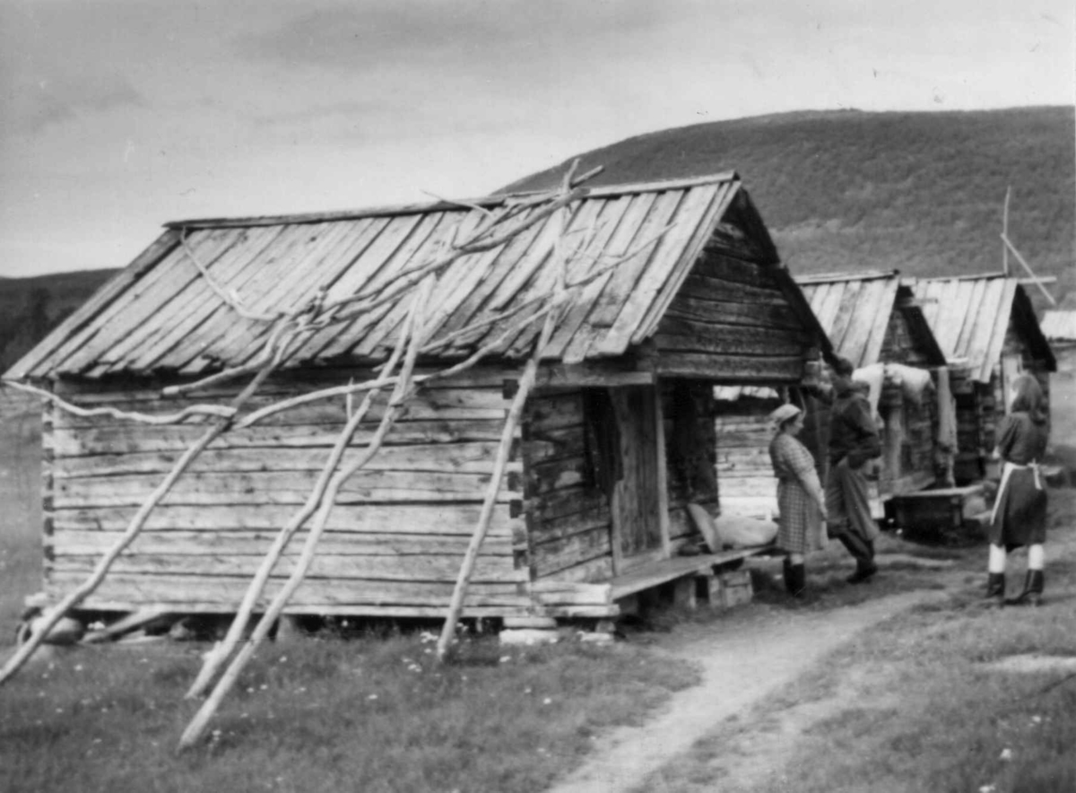 Tre stabbur på gården til Samuel Mikkelsen., utenfor står fru Samuel Mikkelsen, H. Eidheim og Anna Kirsten Mikkelsen. Levajokgiedde 1952.