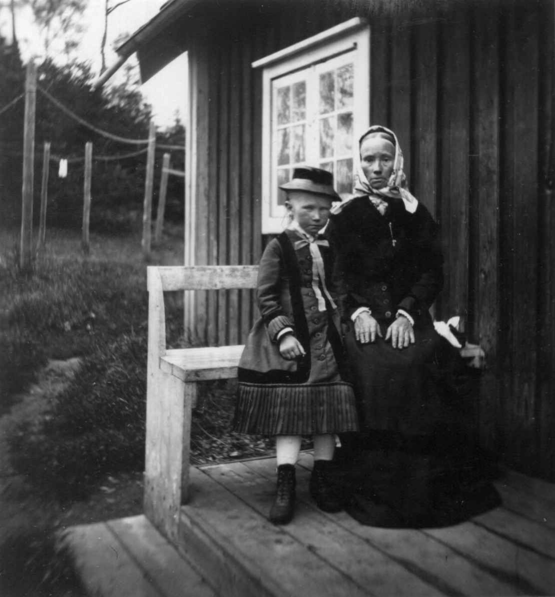 Husmannsfolk, kvinne og pike på benk foran hus. 
Fra portrettserie av personer som bodde på eller besøkte Dal gård, Ullensaker, fotografert av gårdens eier, kammerherre Fredrik Emil Faye (1844-1903) i årene 1875-1900.