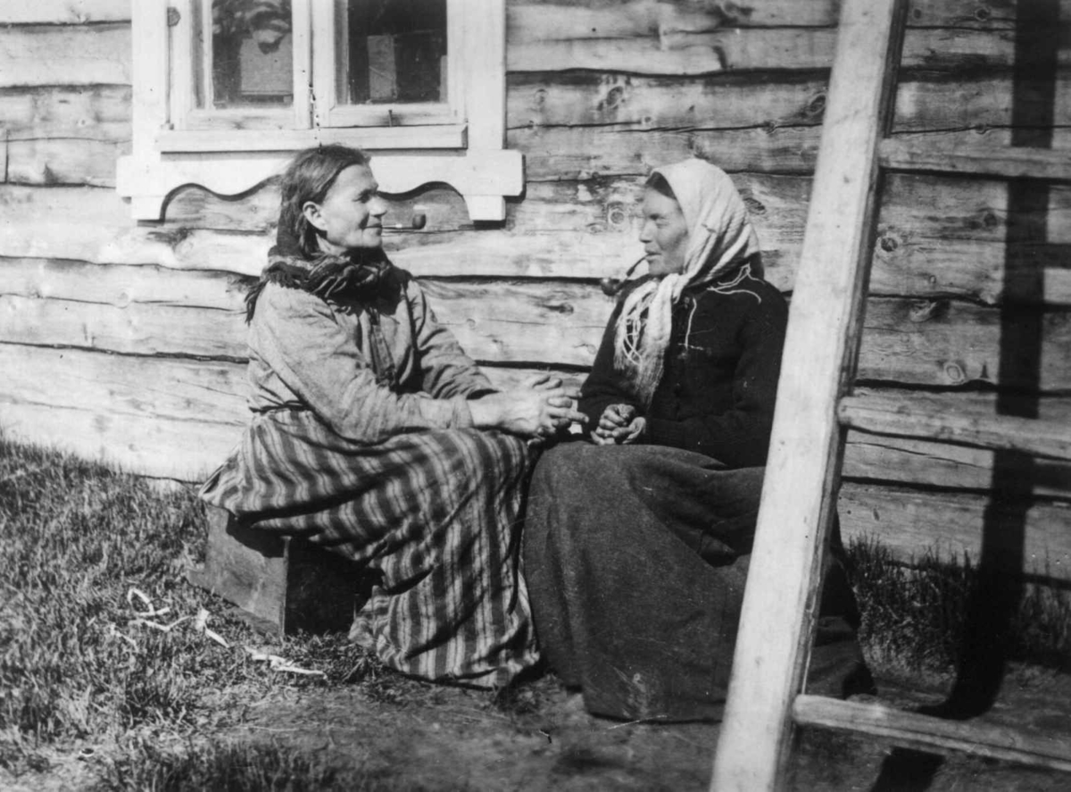 Finske kvinner ved husvegg med piper. Neiden, Sør-Varanger, Finnmark, antatt 1900-1910.