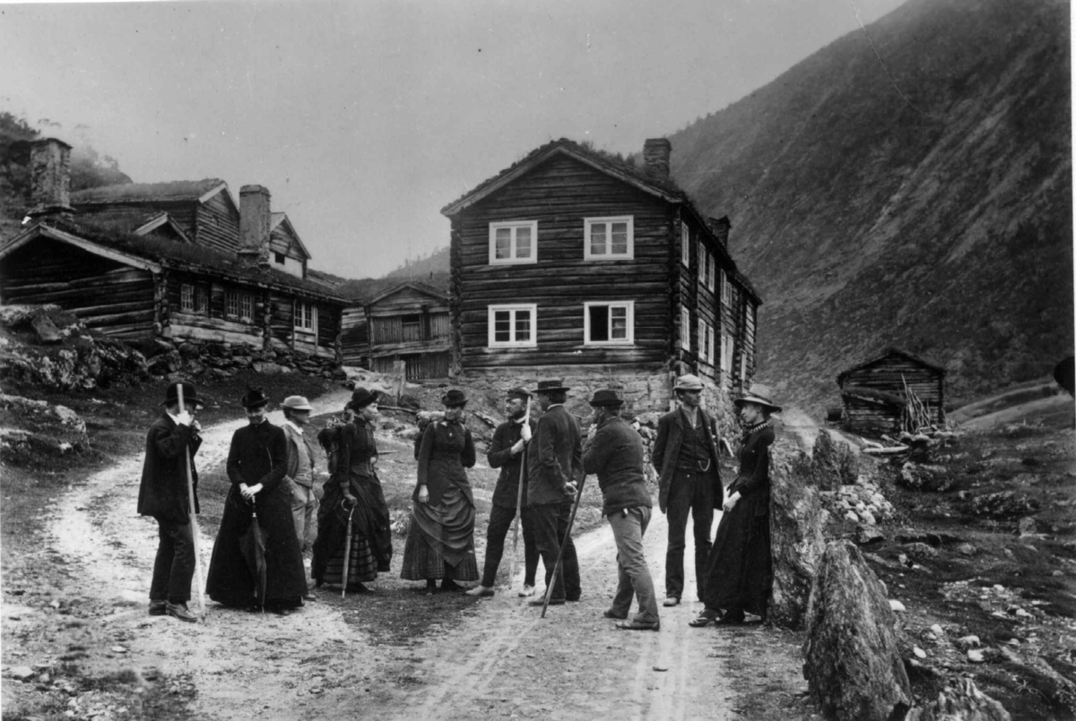 Persongruppe i turdrakter med foran Røysheim, Bøverdalen, Lom, Oppland, antatt juli 1886 da Axel Lindahl var på stedet..