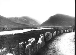 Landskap, ukjent sted. Utsyn over sjø/elv omkranset av fjell