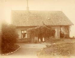 Barn stående foran trebygning ved sjøen, bolig, ukjent sted.