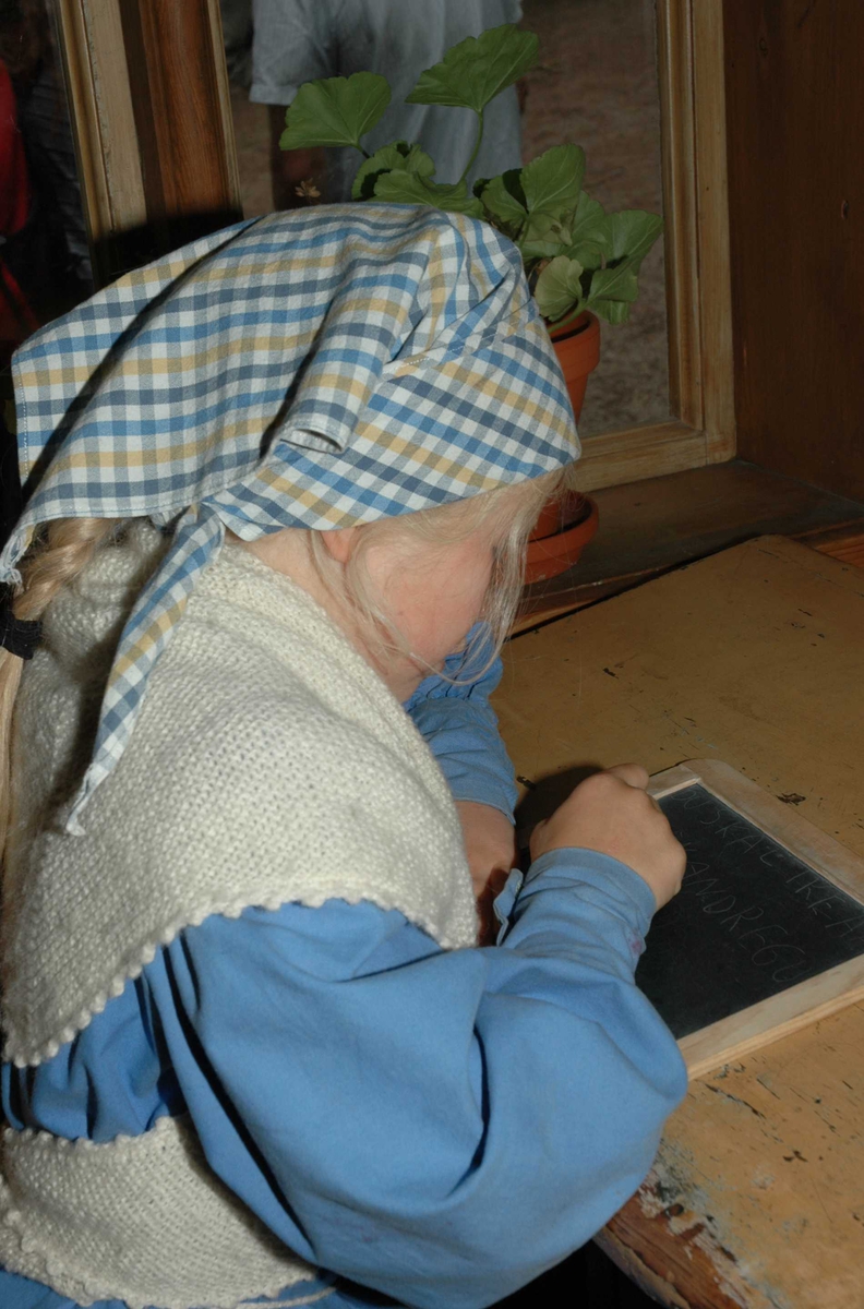 Levendegjøring på museum.
Ferieskolen uke 32 i 2005. Jente i drakt øver seg på å skrive. 
Norsk Folkemuseum, Bygdøy.