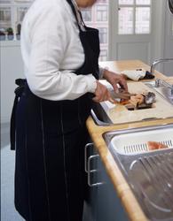 En dame står ved kjøkkenbenken og tilbereder mat. llustrasjo