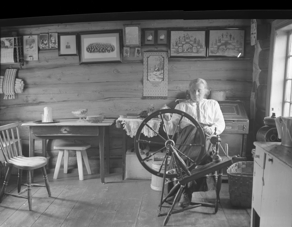 Interiør, Blokkhusmorka, Lønset, Oppdal, Sør-Trøndelag. Kvinne sitter og spinner på rokk. Fotografert 1940. 
