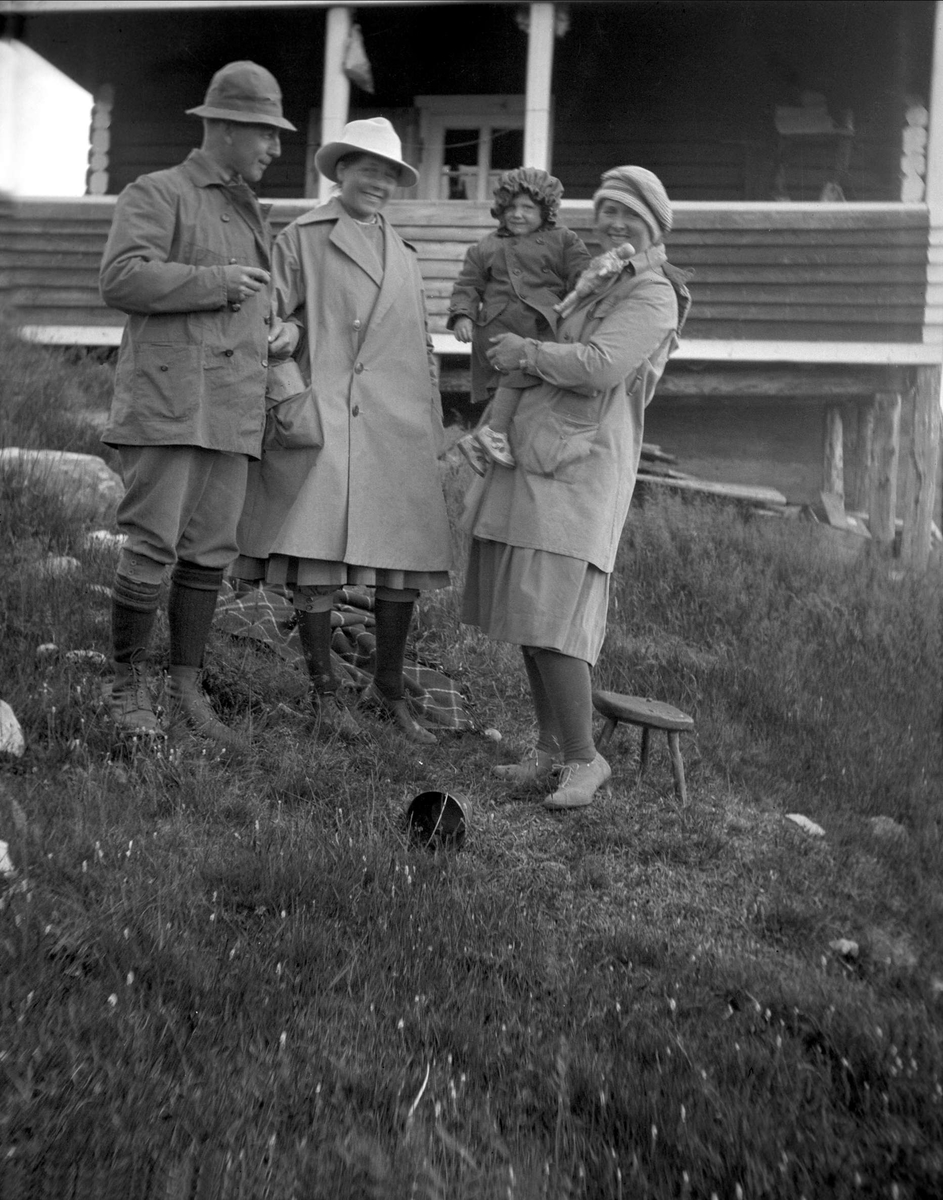 Tre voksne og et barn står foran et hus. Robsahm og Lund.