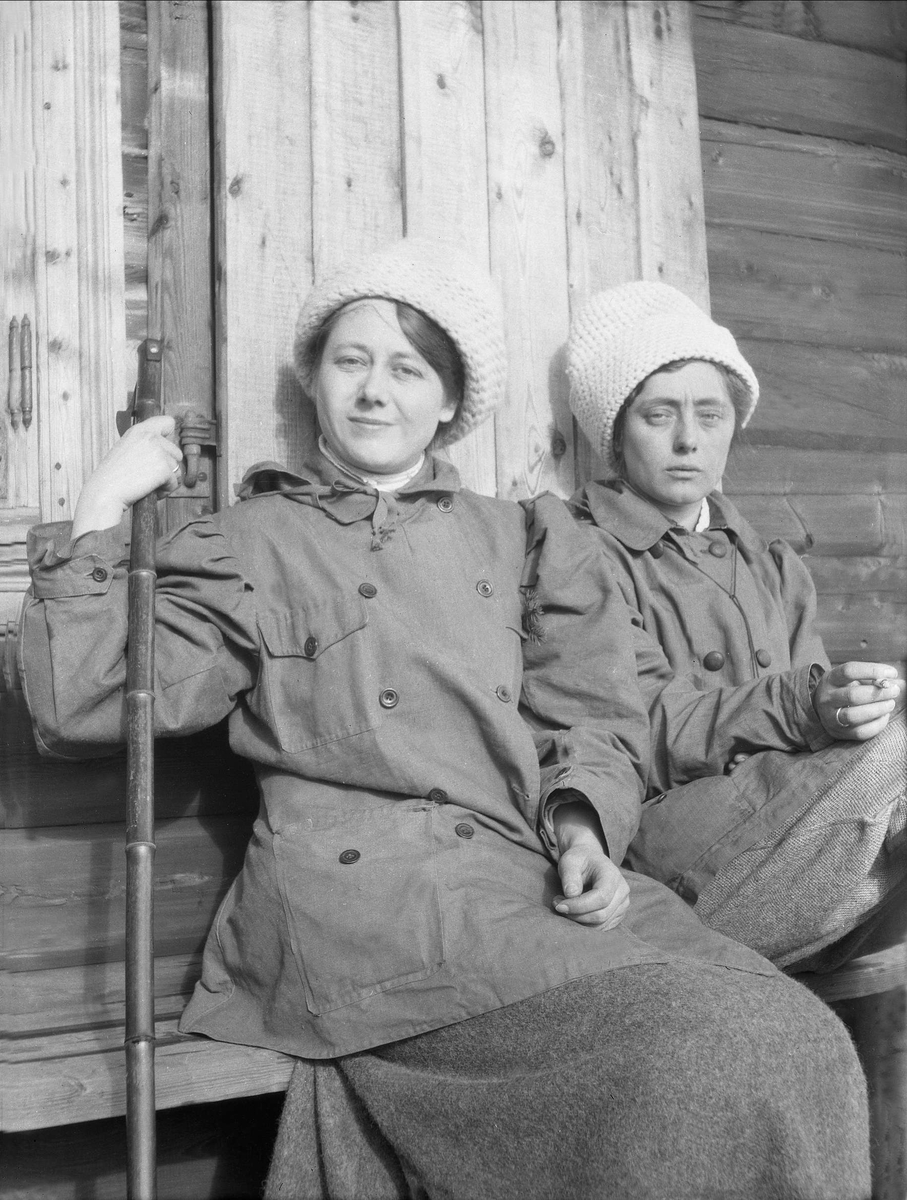 To kvinner sitter utenfor en husvegg. Robsahm og Lund.