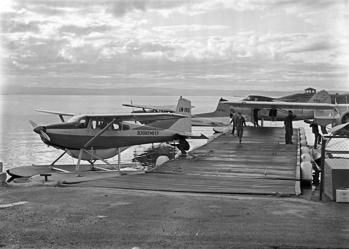 To småfly fra Bjørumfly A/S og et fra Fjellfly A/S ligger ved Fornebu sjøflyhavn. Fotografert august 1962.