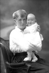 Gruppeportrett, sittende kvinne med spedbarn i fanget. Fru G