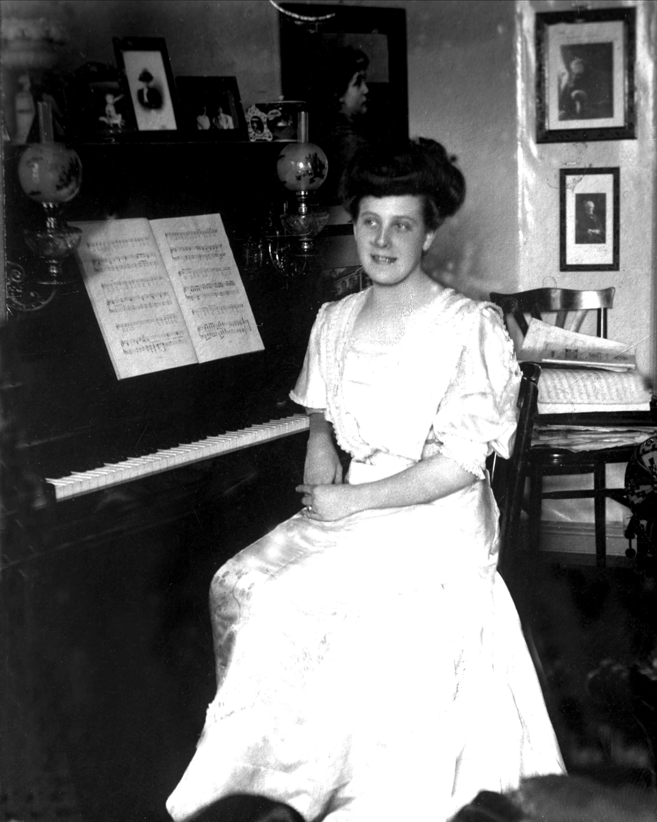 Avfotografering.
Portrett, kvinne i interiør, sittende ved piano. Avfotografert 1915.