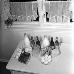 Egg, øl, ost, meierismør og kjøtt. Bord og skap med mat og d