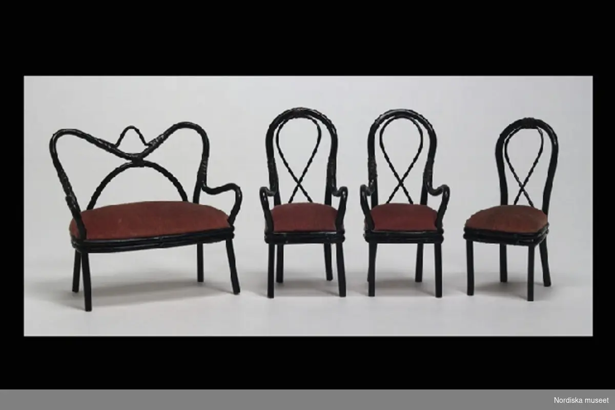 Inventering Sesam 1996-1999:
Möblemang till dockskåp bestående av soffa och 4 st stolar, Thonet-modell, tillverkade av svartmålad rotting, sitsar klädda med röd sammet. 
a) Soffa L 9,5   H 9,5  (cm)
b-c) 2 st  karmstolar H 10 cm
d-e) 2 st stolar H 9,5 cm. 
Tillhör dockskåp från omkr 1840, inv nr 145.505, inrett 1872 av leksakshandlare W A Bandel, Västerlånggatan, Stockholm, för dottern Thyra, vilken vid överlämnandet till museet själv gjort uppställningen av föremålen i dockskåpet.
Birgitta Martinius 1997